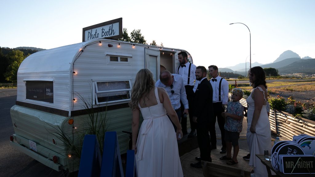 Wedding guests gathered outside a vintage photo booth trailer at sunset