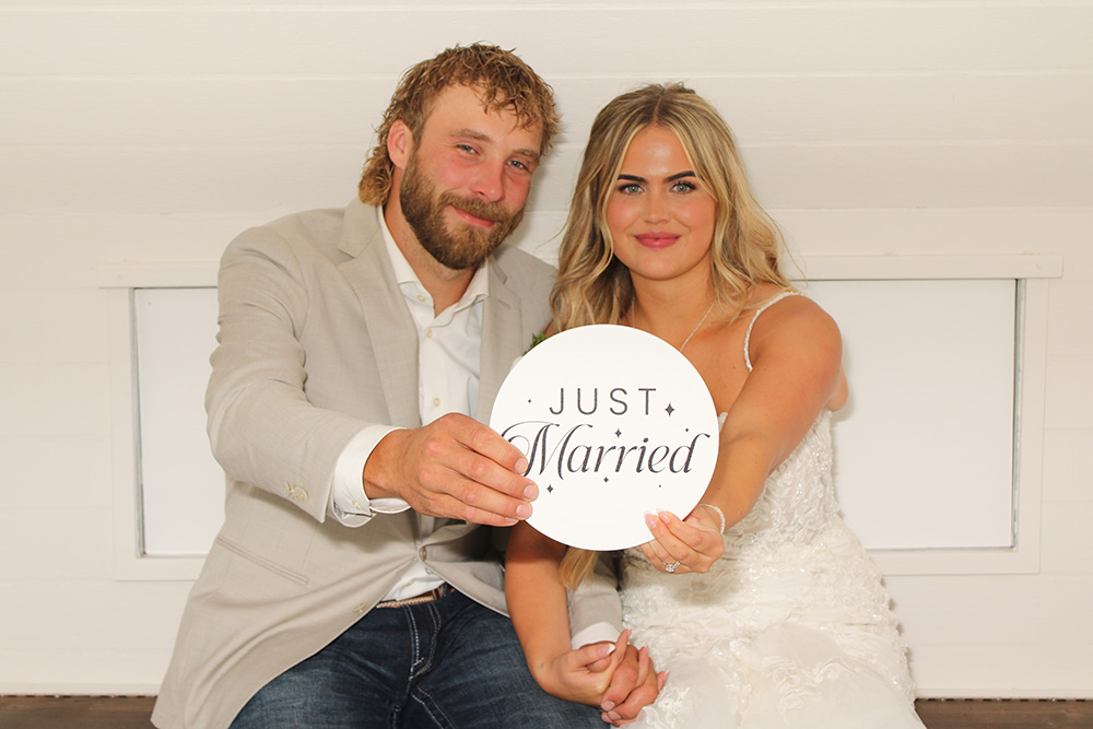 Bride and groom holding a “Just Married” sign while posing inside a photo booth